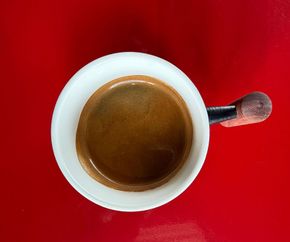 A cup of cappuccino is sitting on a red saucer on a wooden table.