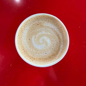 A red cup of cappuccino is sitting on a red surface