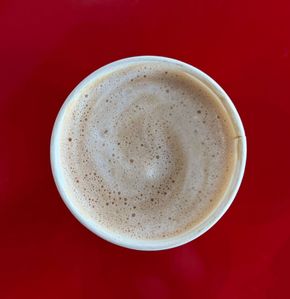A red cup of cappuccino on a saucer on a wooden table.