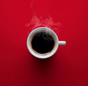A cup of coffee with steam coming out of it on a red background