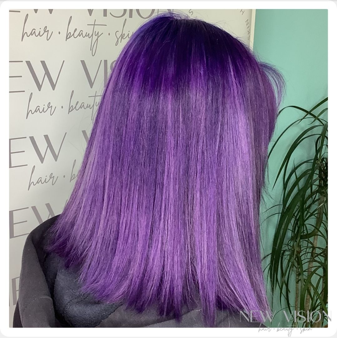 A woman with purple hair is standing in front of a sign that says hair beauty.