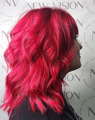 A woman with bright red hair is standing in front of a wall.