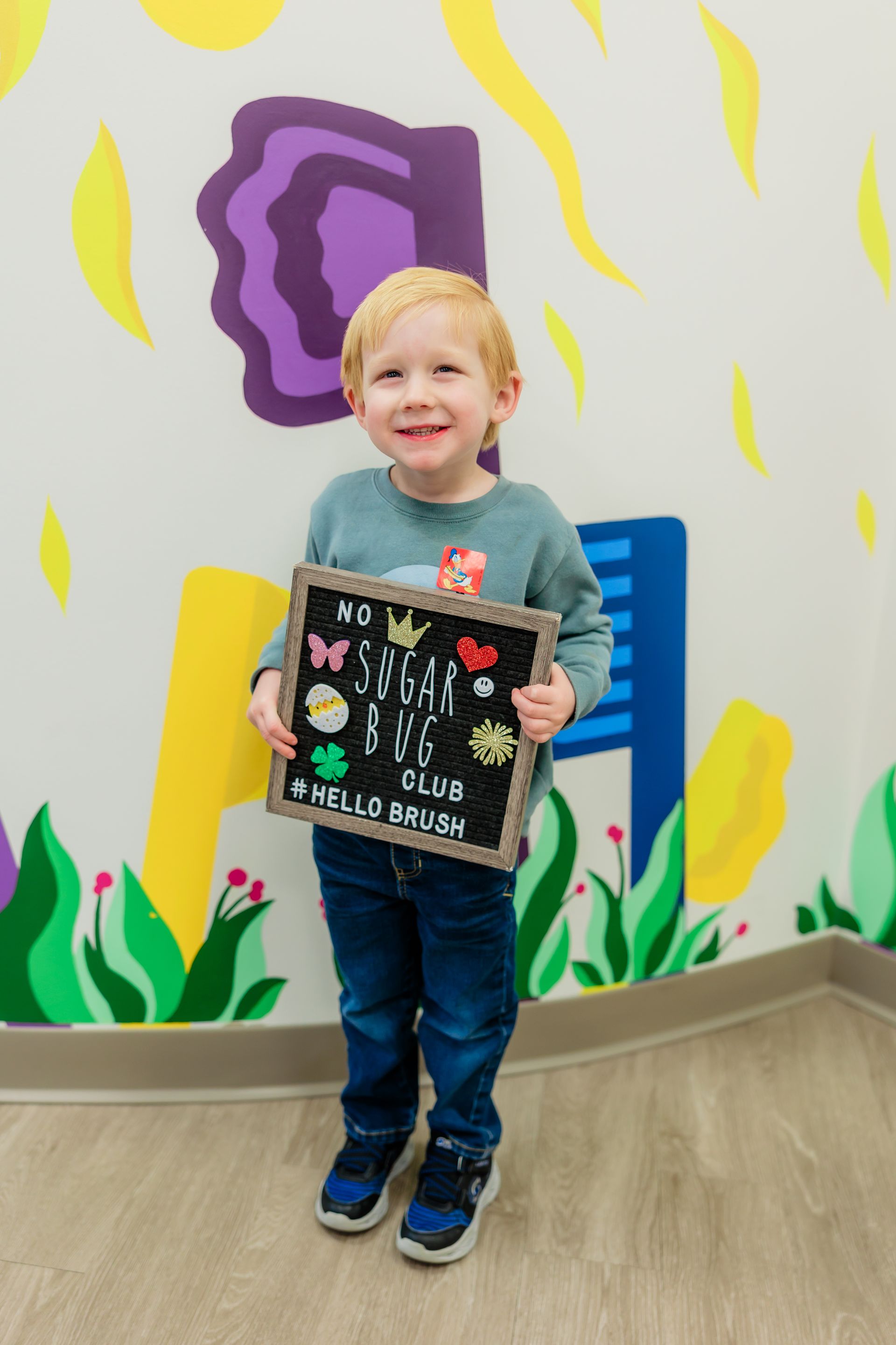 A young boy is holding a chalkboard in front of a colorful wall.