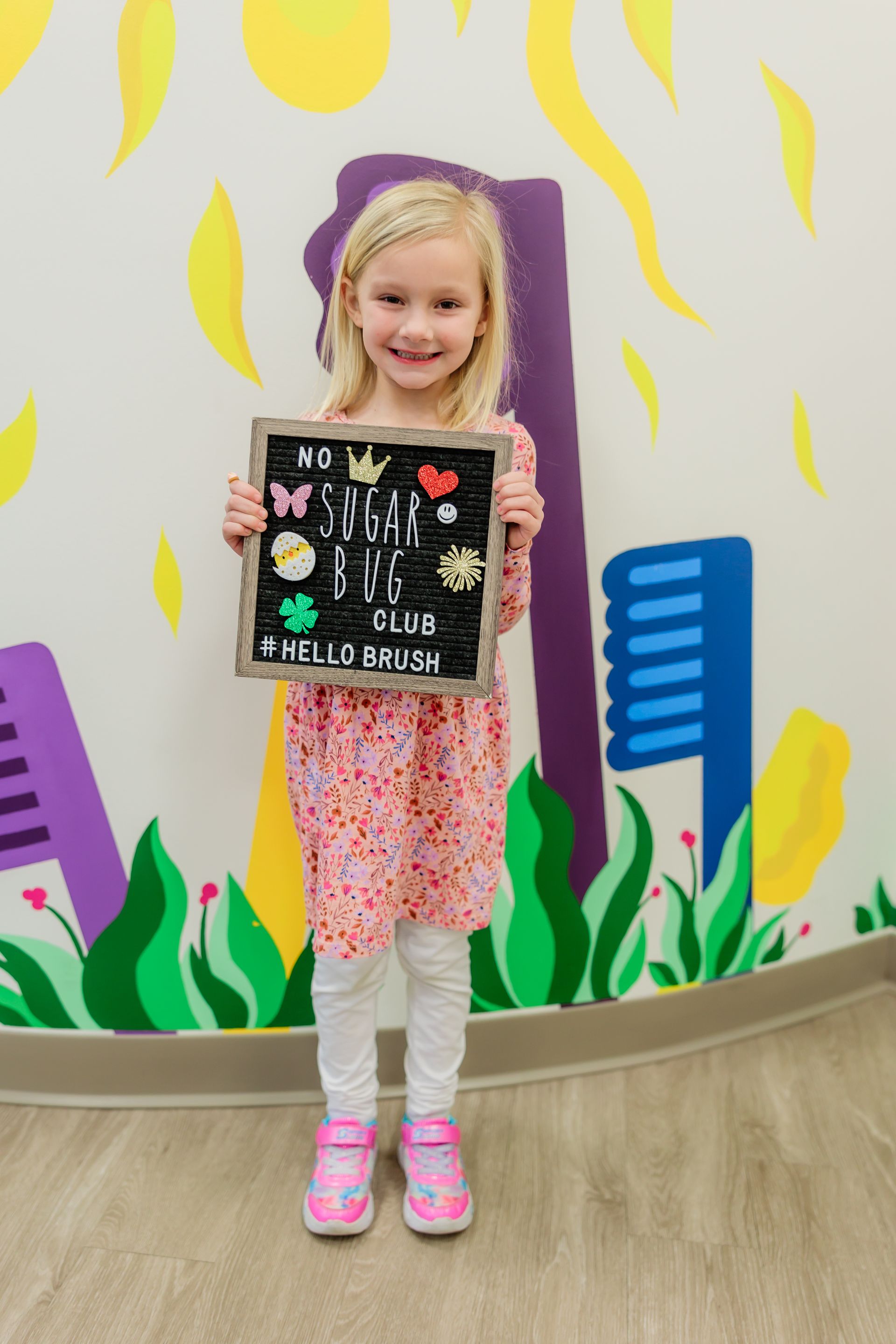 A little girl is holding a chalkboard in front of a colorful wall.