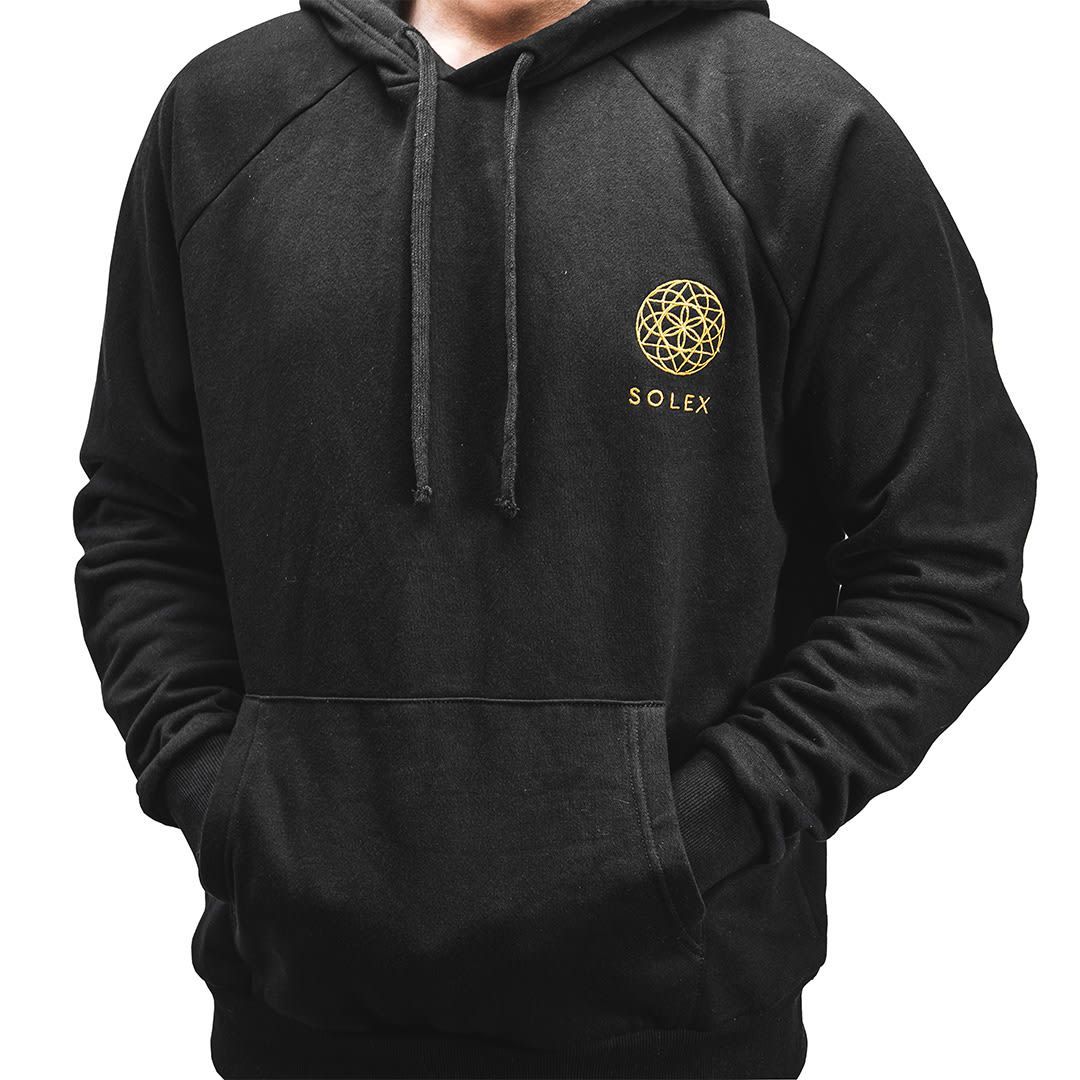 Black hoodie with gold logo on chest, hands in front pocket.