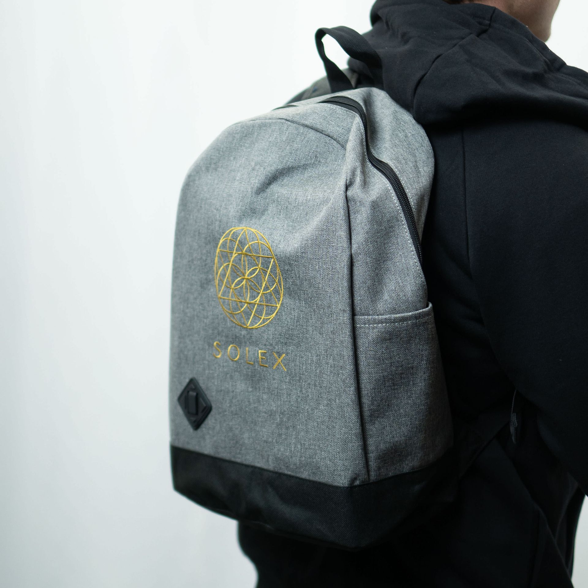 Person wearing a gray backpack with gold emblem and "SOLEX" text. Black bottom and small pocket.