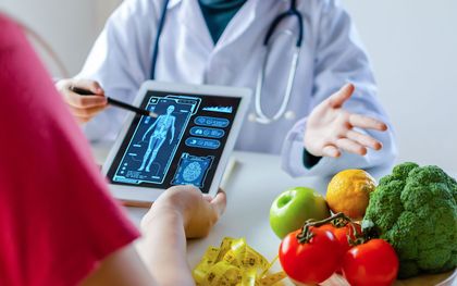 Doctor showing a body scan on a tablet to a patient, with fresh produce on the table.