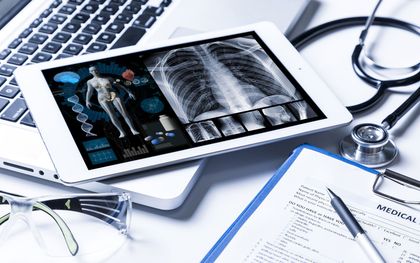 Tablet displaying medical scans, with a laptop, stethoscope, and paperwork.