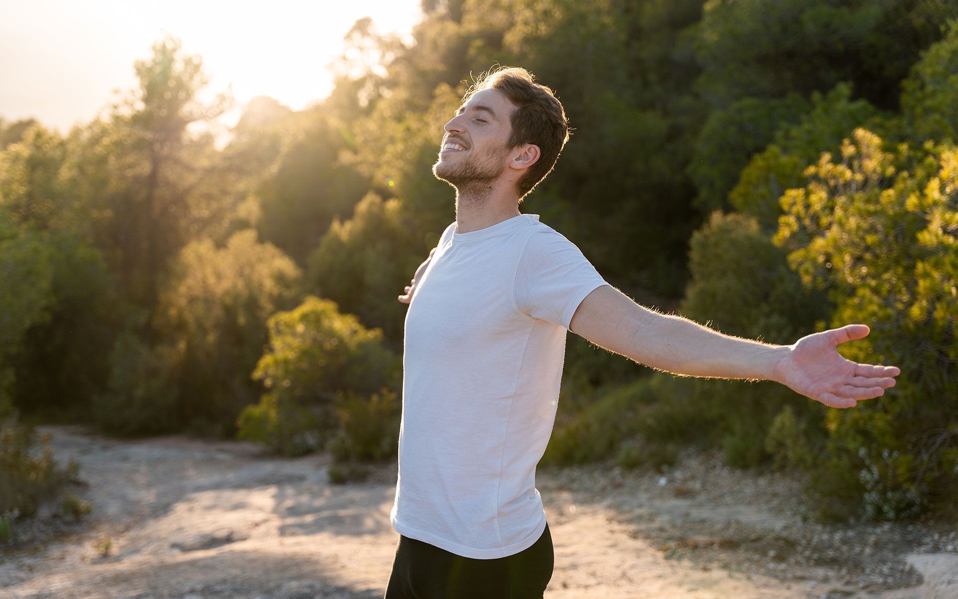 Man with arms outstretched, eyes closed, basking in sunlight outdoors.