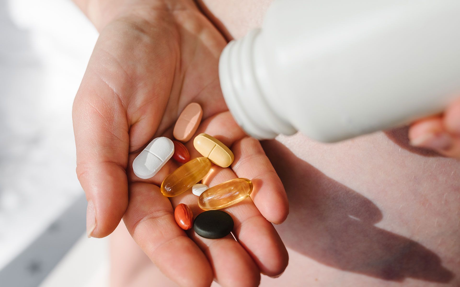 Hand holding various pills, pouring more from a white bottle.