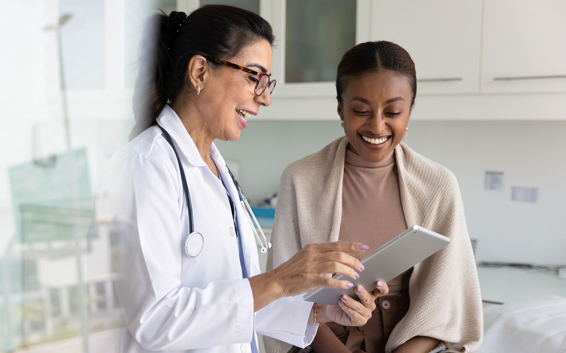 Doctor showing tablet to a smiling patient in a brightly lit medical office.