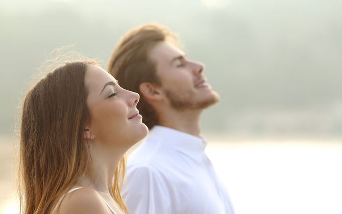 Woman and man with eyes closed, heads tilted back, smiling outdoors.