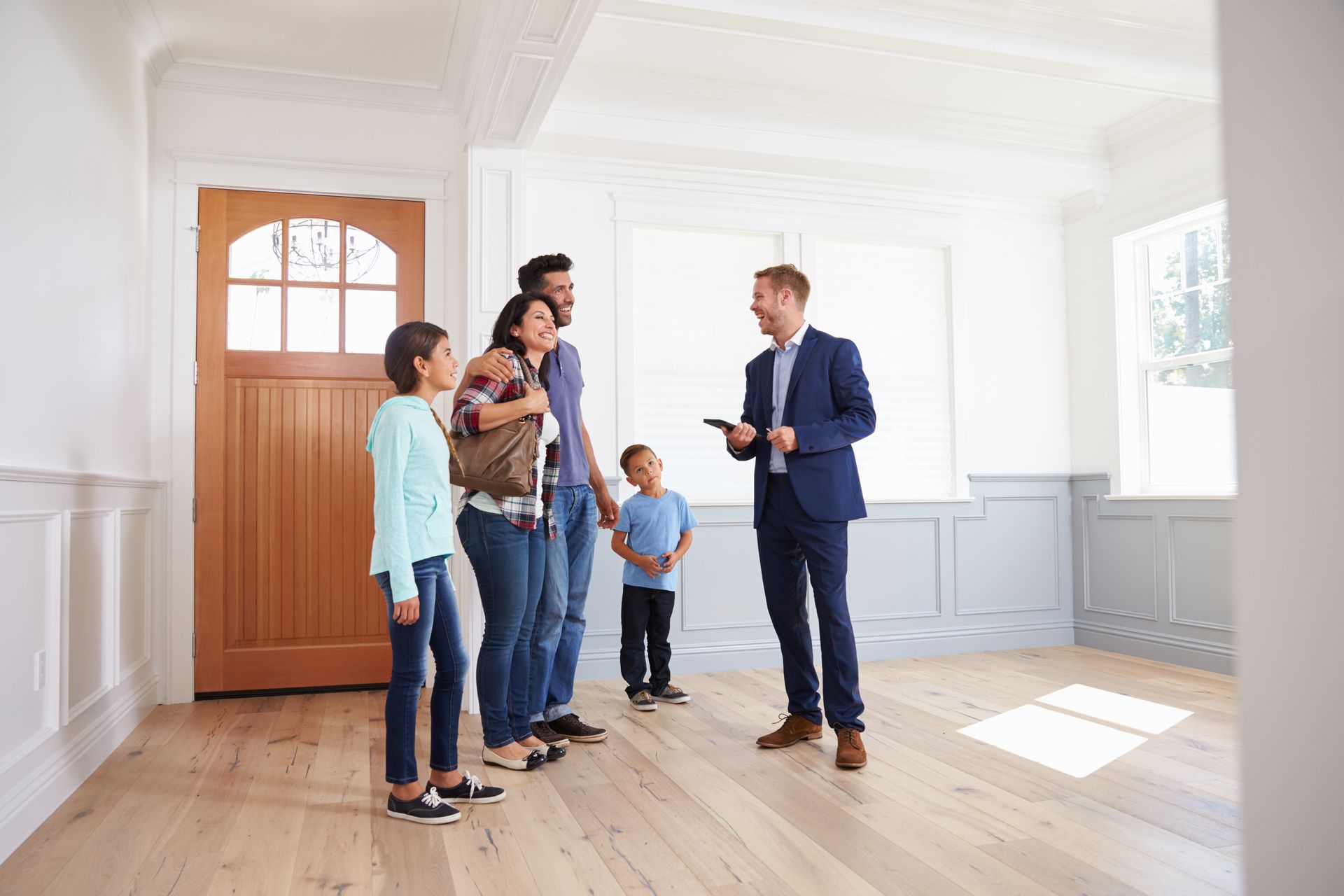 A real estate agent talks with a family inside the light-filled entryway of an empty home with wood floors.
