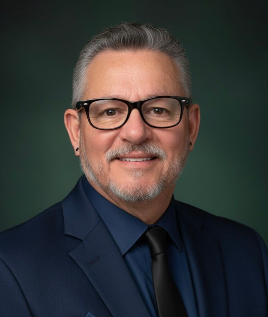 Two people in business attire shake hands over a document on a desk with two small model houses.
