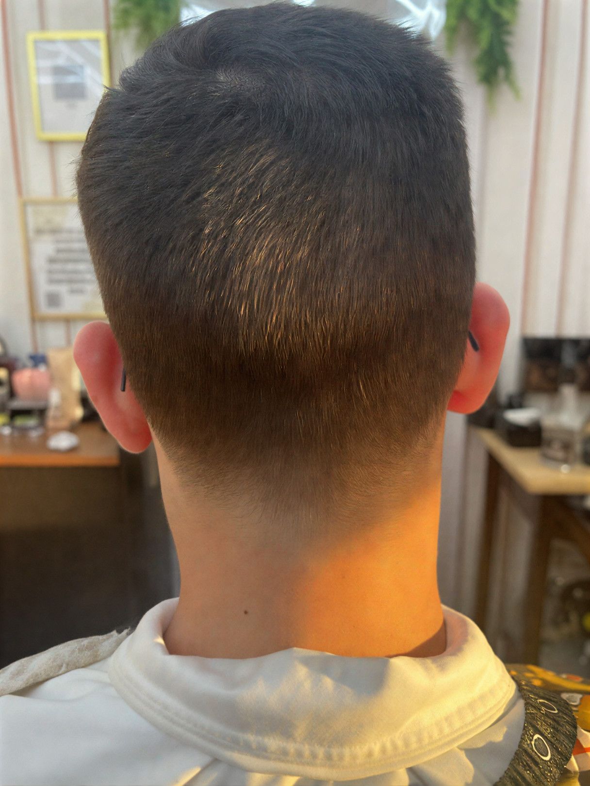 Person's back of head showing a dark, short haircut with a faded neckline, near an ear with glasses.