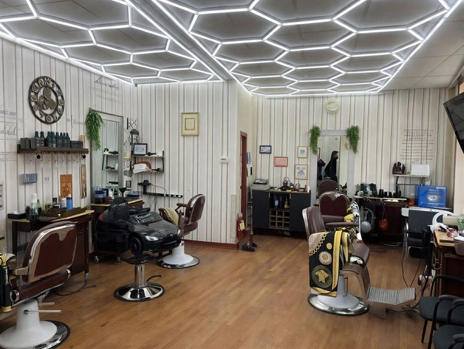 Barbershop interior with barber chairs, wood panel walls, honeycomb ceiling lights, and grooming products.