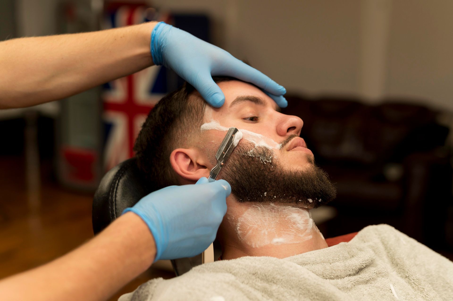 A man is getting his beard shaved by a barber in a barber shop.