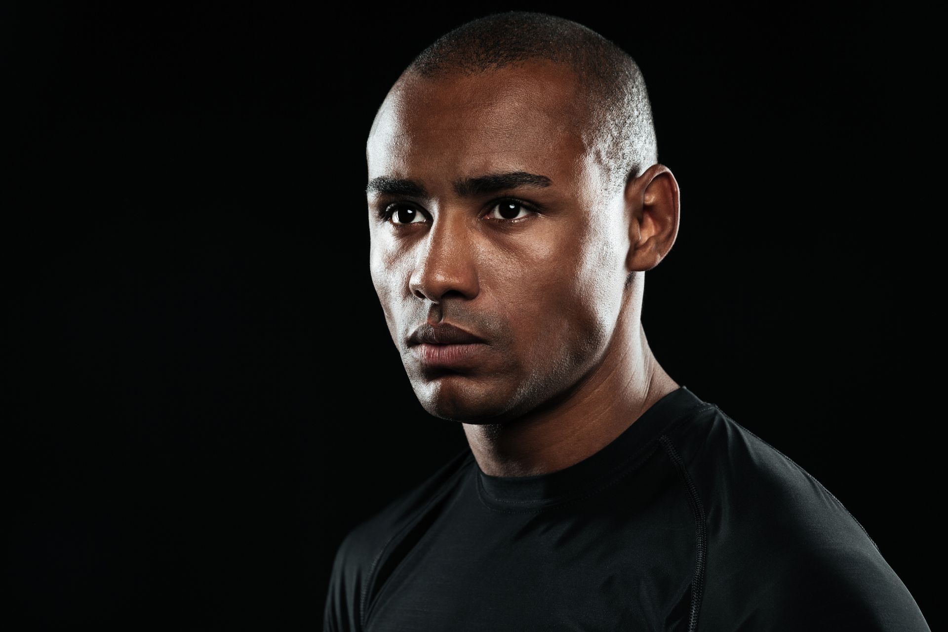 A man in a black shirt is looking at the camera on a black background.