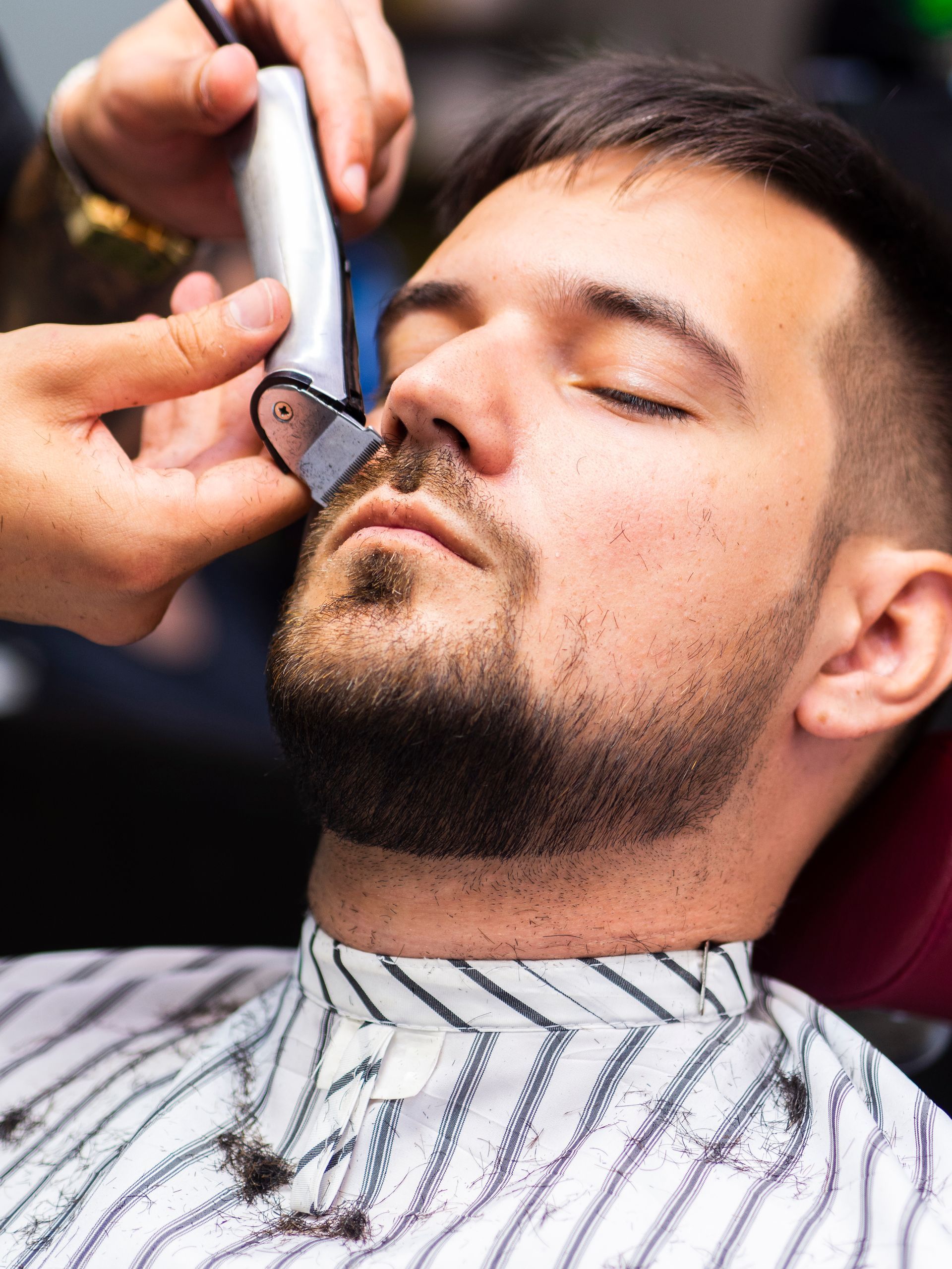 A man is getting his beard shaved by a barber with a razor.