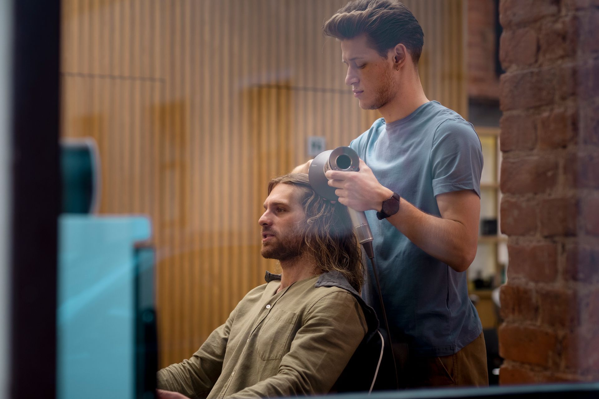 A man is getting his hair blow dried by a hairdresser in a salon.