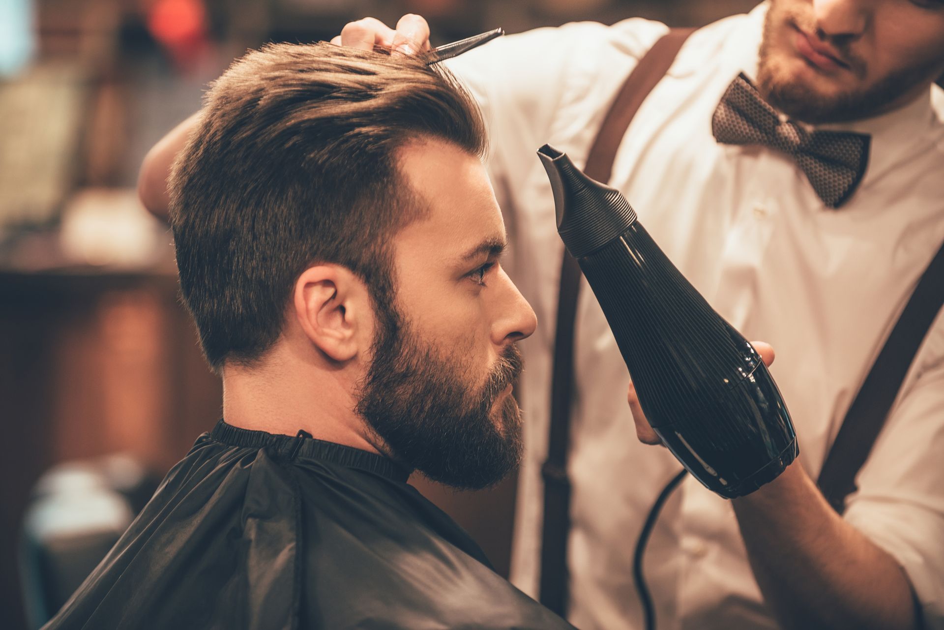 A man is getting his hair blow dried by a barber.