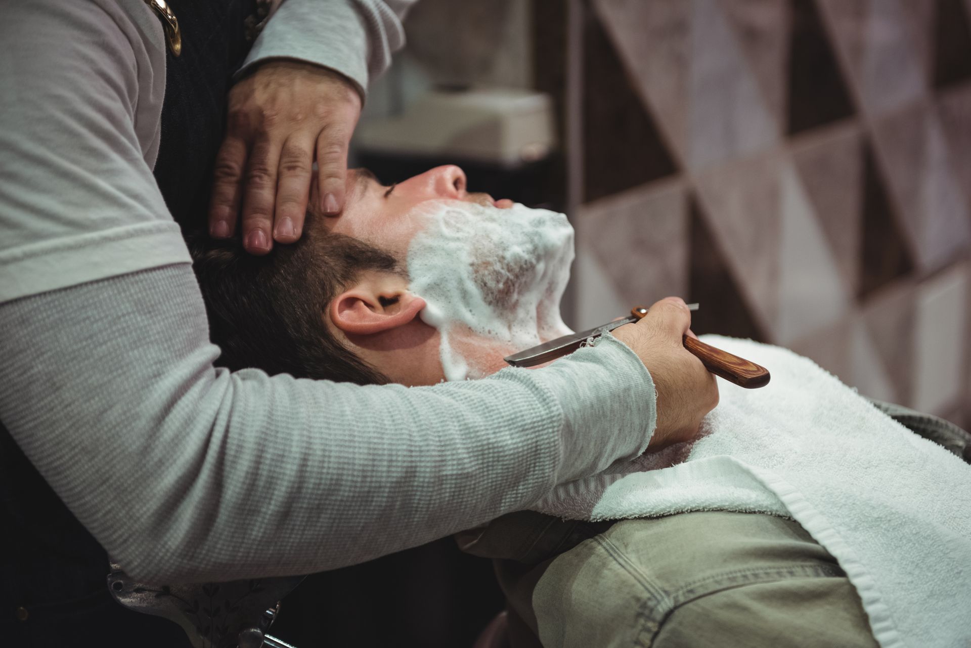 A man is getting his beard shaved by a barber in a barber shop.