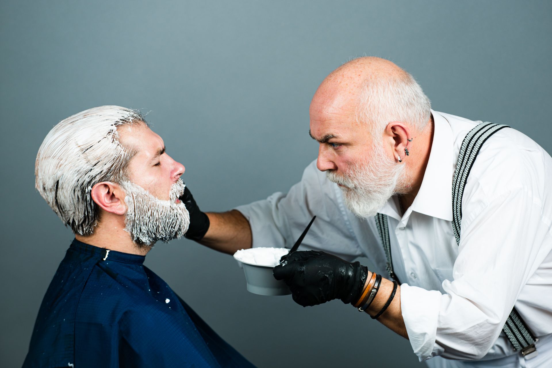A man with a beard is getting his hair dyed by a barber.