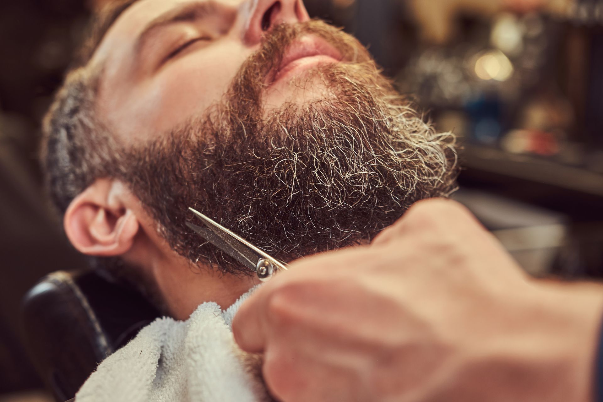 A man is getting his beard shaved by a barber in a barber shop.