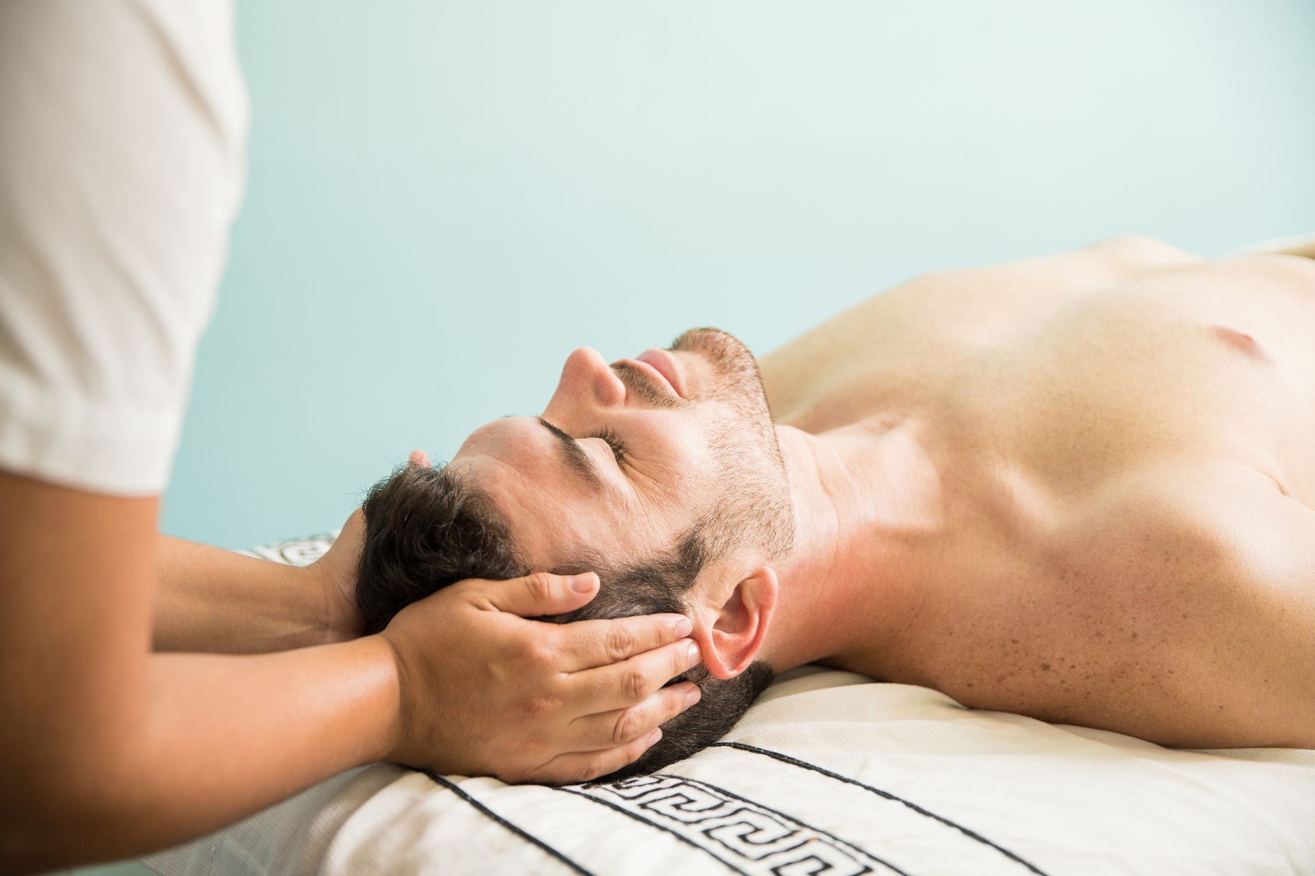 A shirtless man is getting a head massage from a woman.