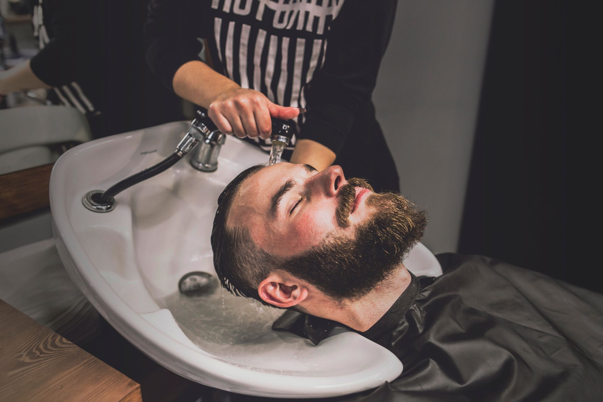 A man is getting his hair washed in a sink at a barber shop.