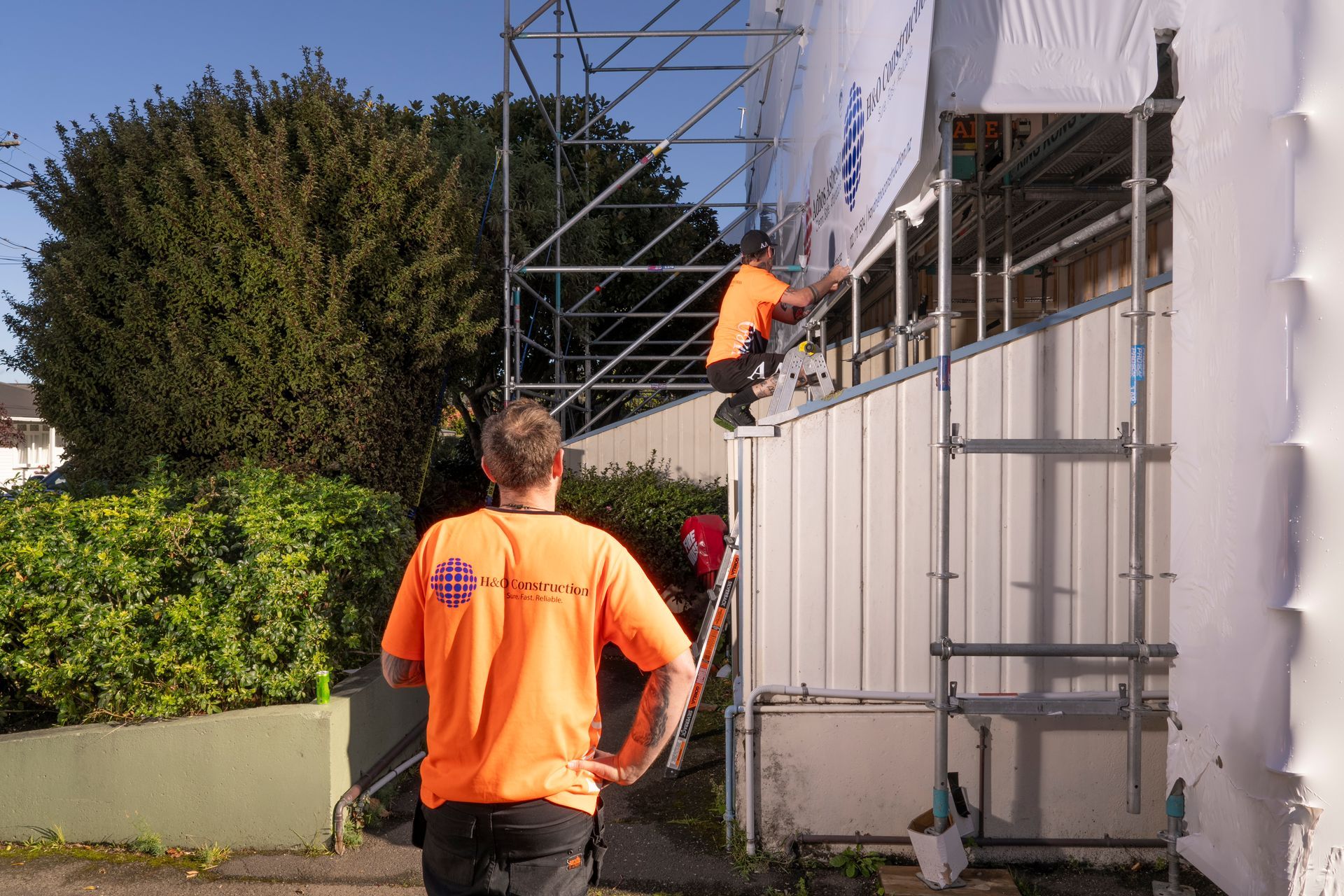 A man in an orange shirt is standing in front of a scaffolding.