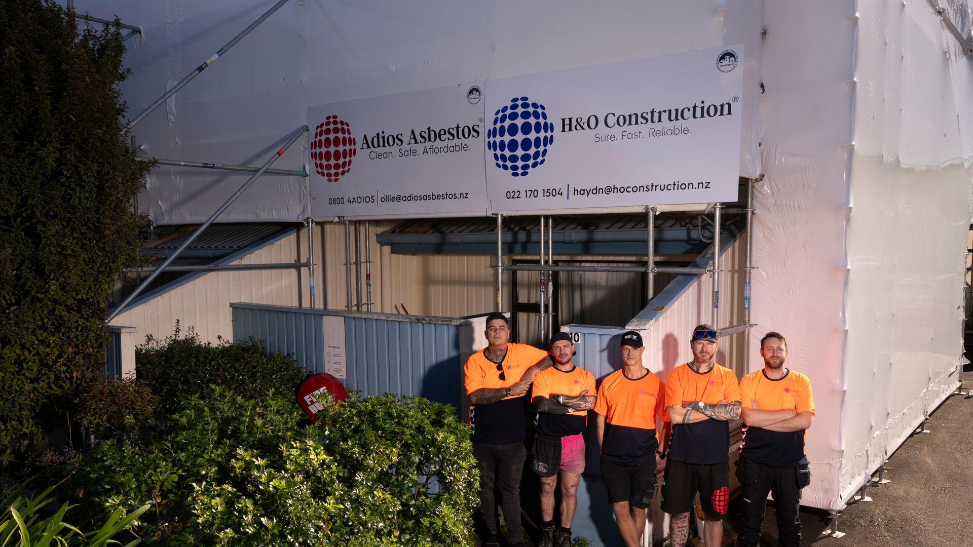 A group of construction workers are posing for a picture in front of a building covered in scaffolding.