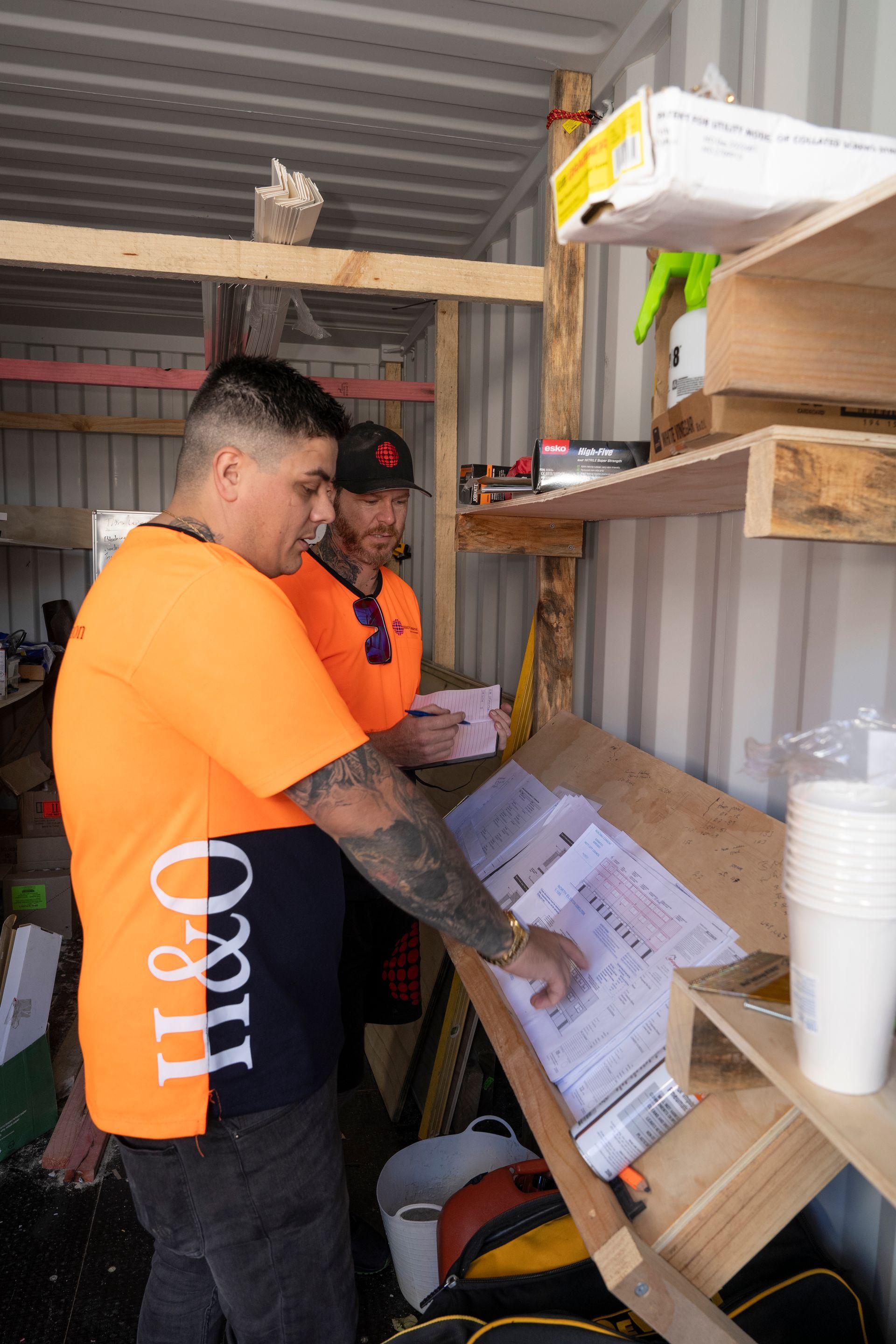 Two men are standing next to each other in a room looking at papers.