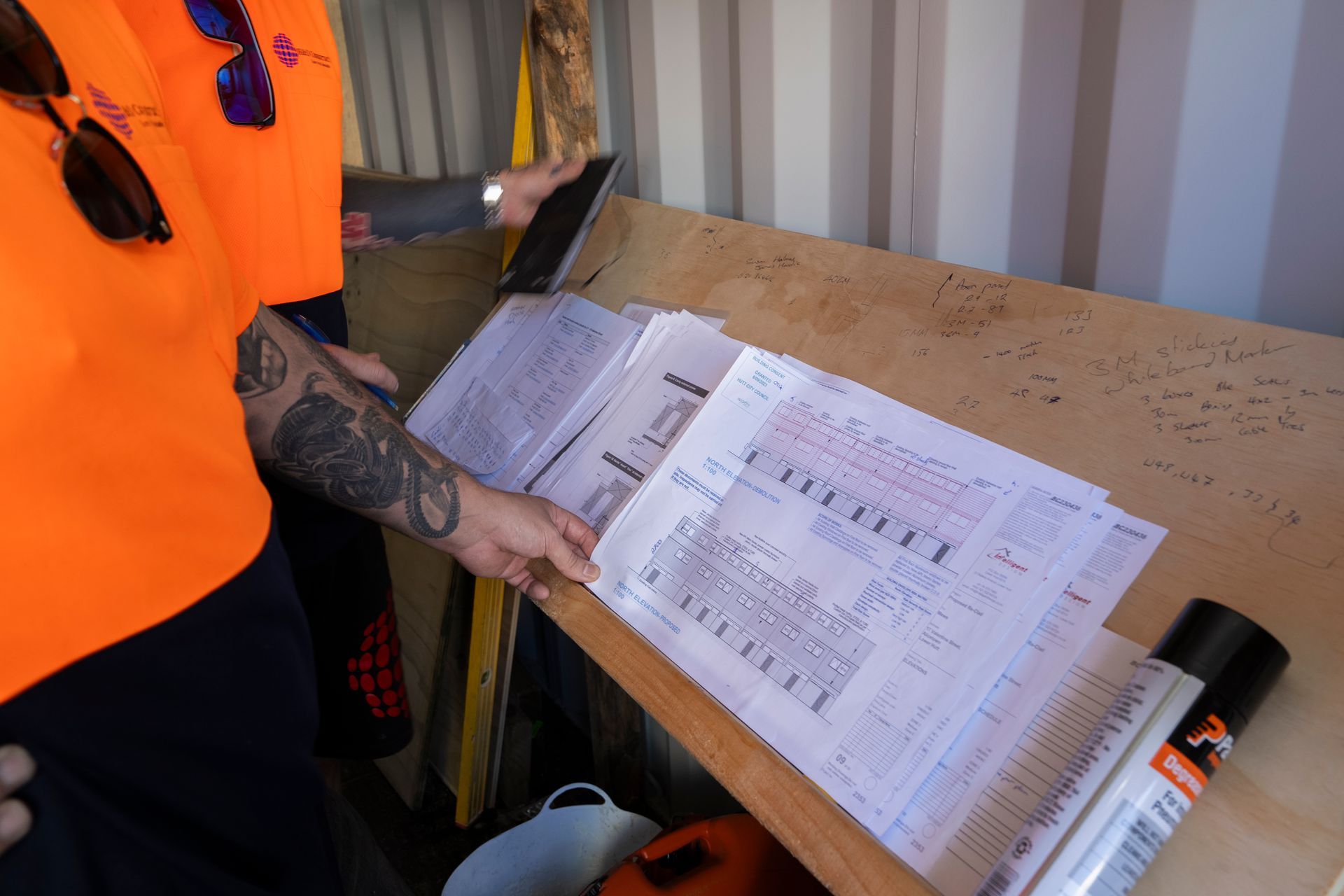 A man in an orange vest is looking at a piece of paper on a table.