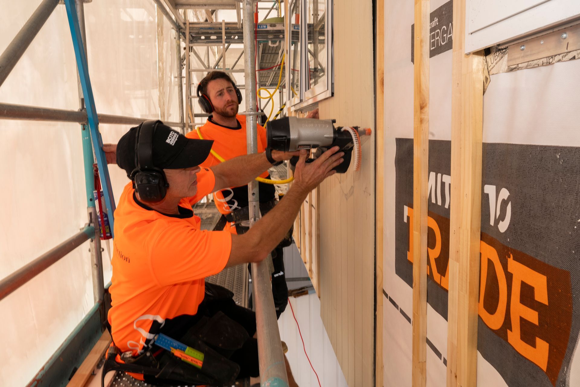 Two men are working on a wall on a scaffolding.