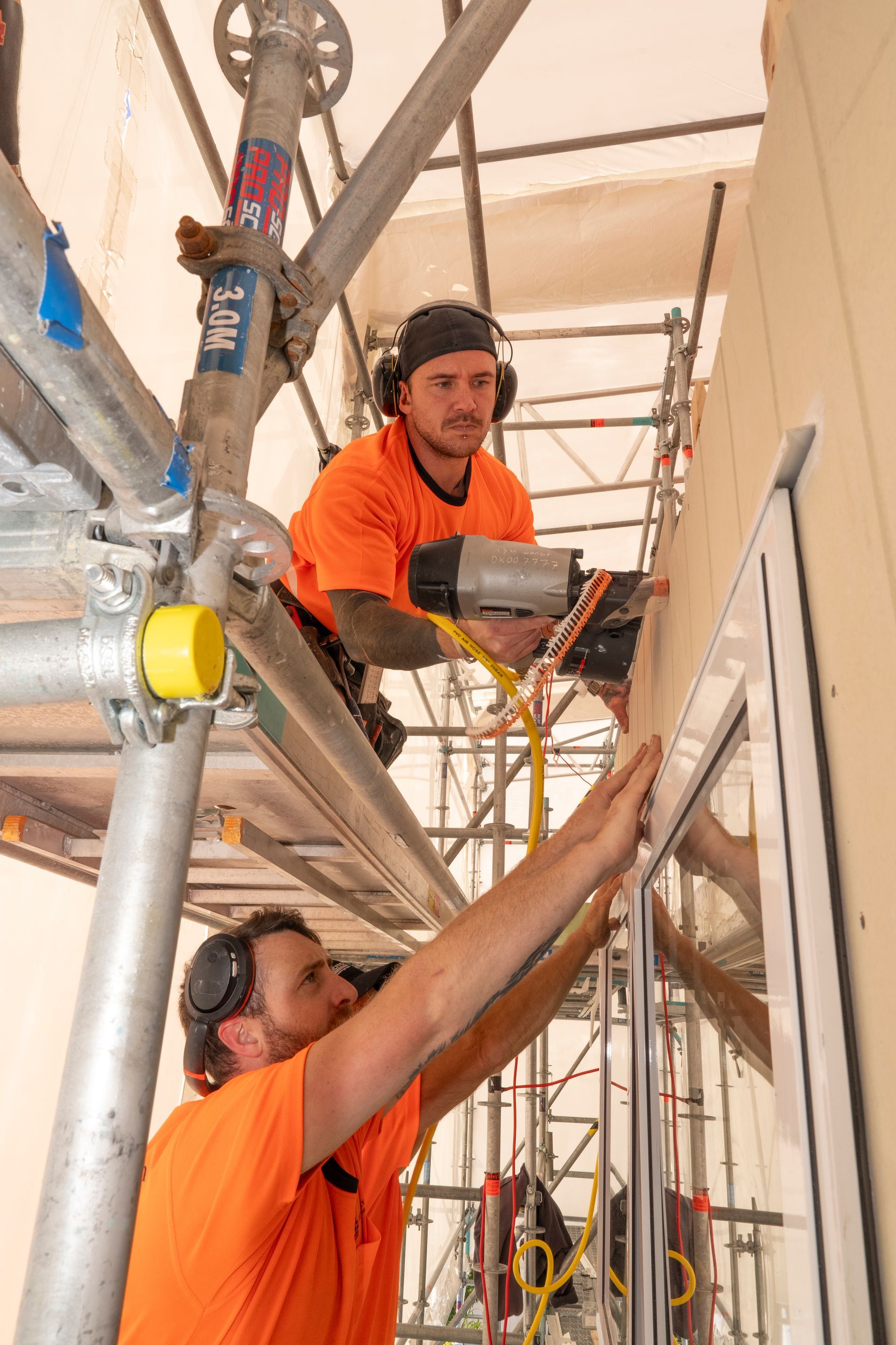 Two men are working on a window on a scaffolding.