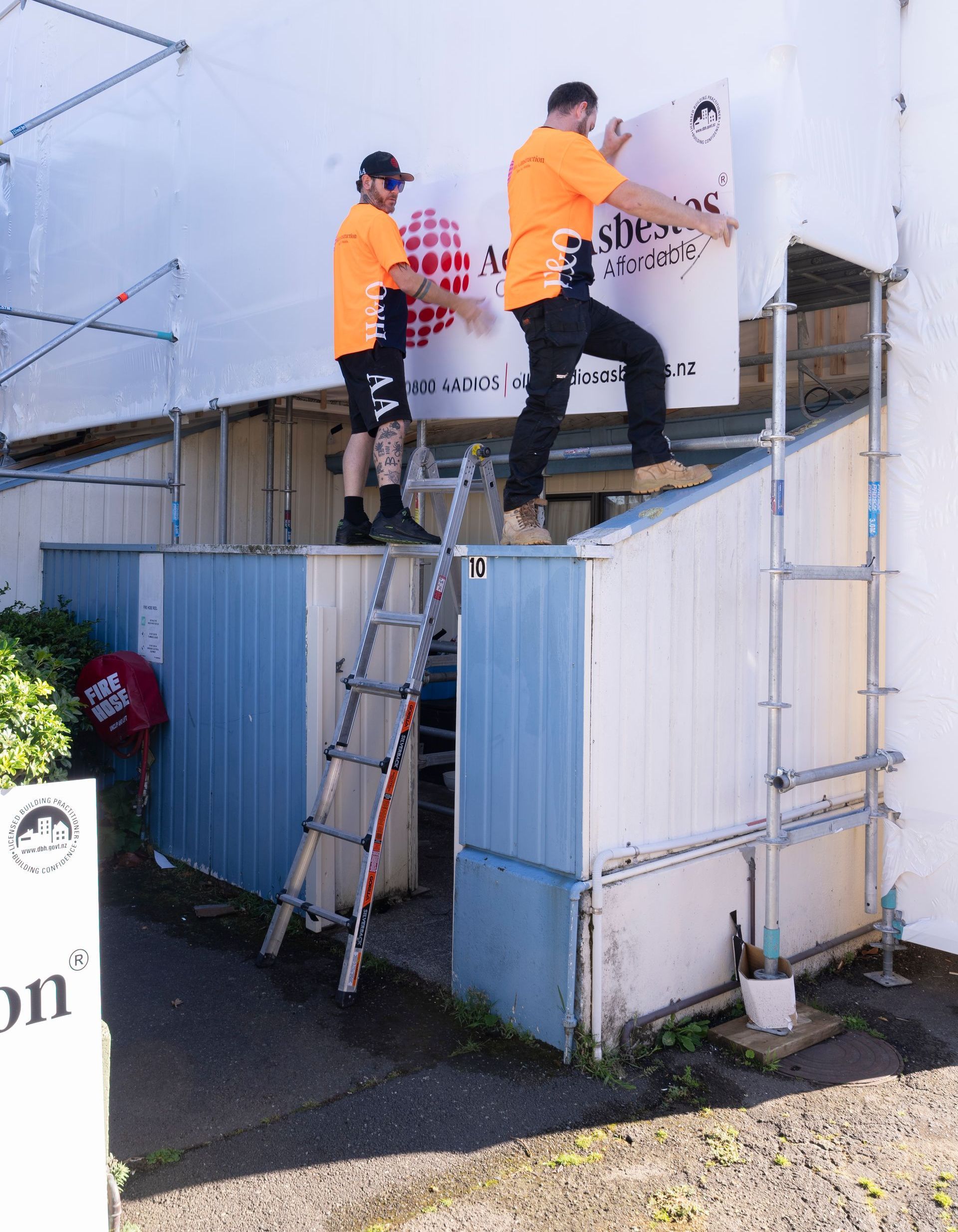 Two men are standing on a ladder painting a sign on a building