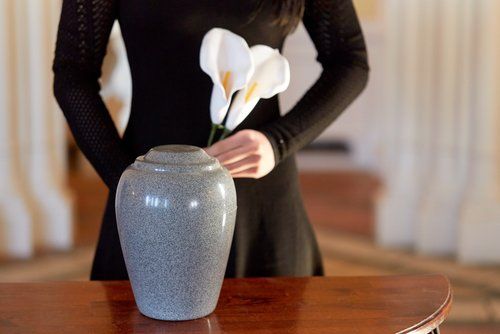 Una persona sistema dei fiori bianchi in un vaso grigio su un tavolo di legno.