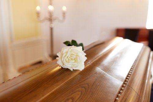 Una rosa bianca su una bara di legno lucido in una cappella illuminata da una luce soffusa.