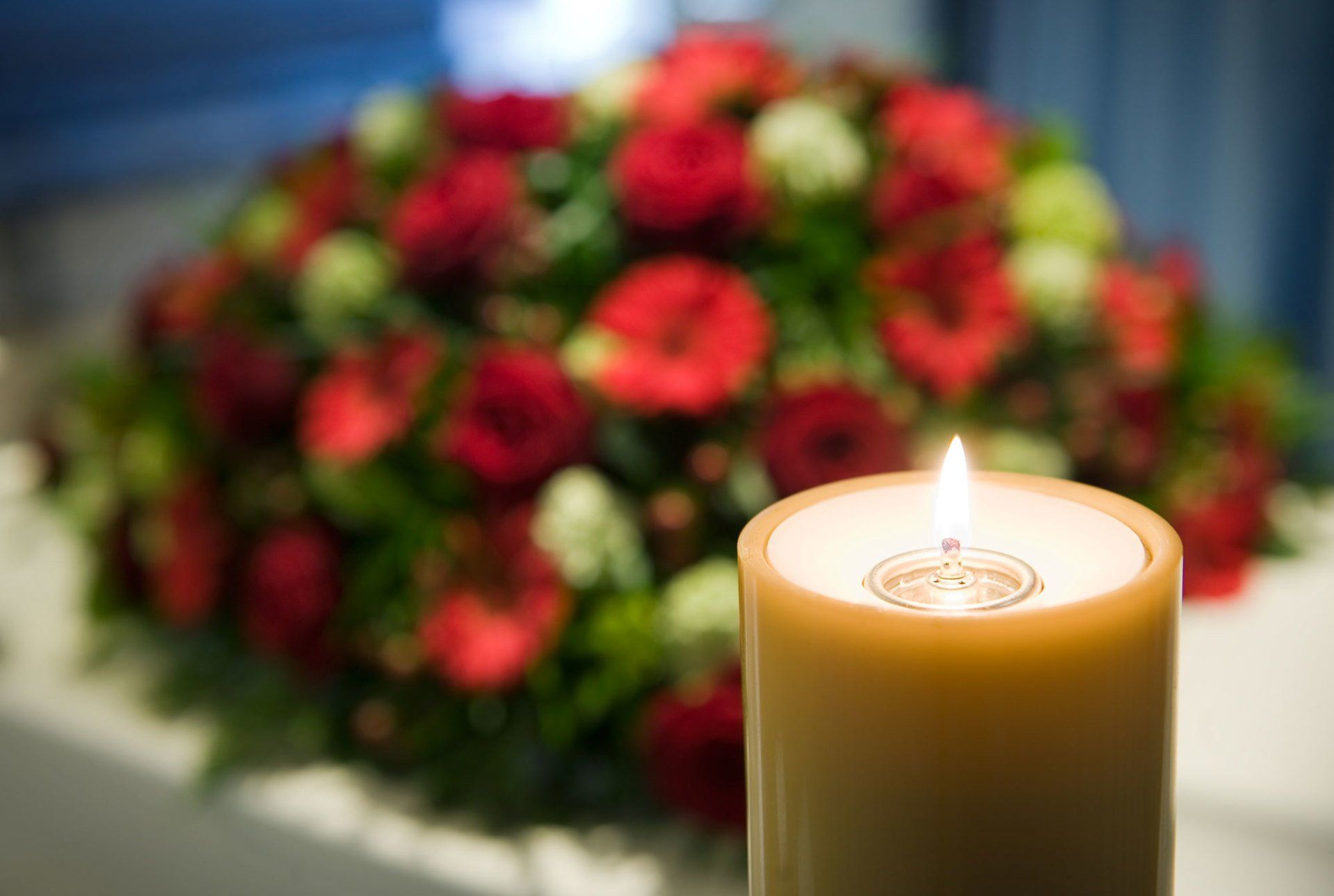 Candela accesa davanti a un omaggio floreale sfocato nei toni del rosso e del rosa.