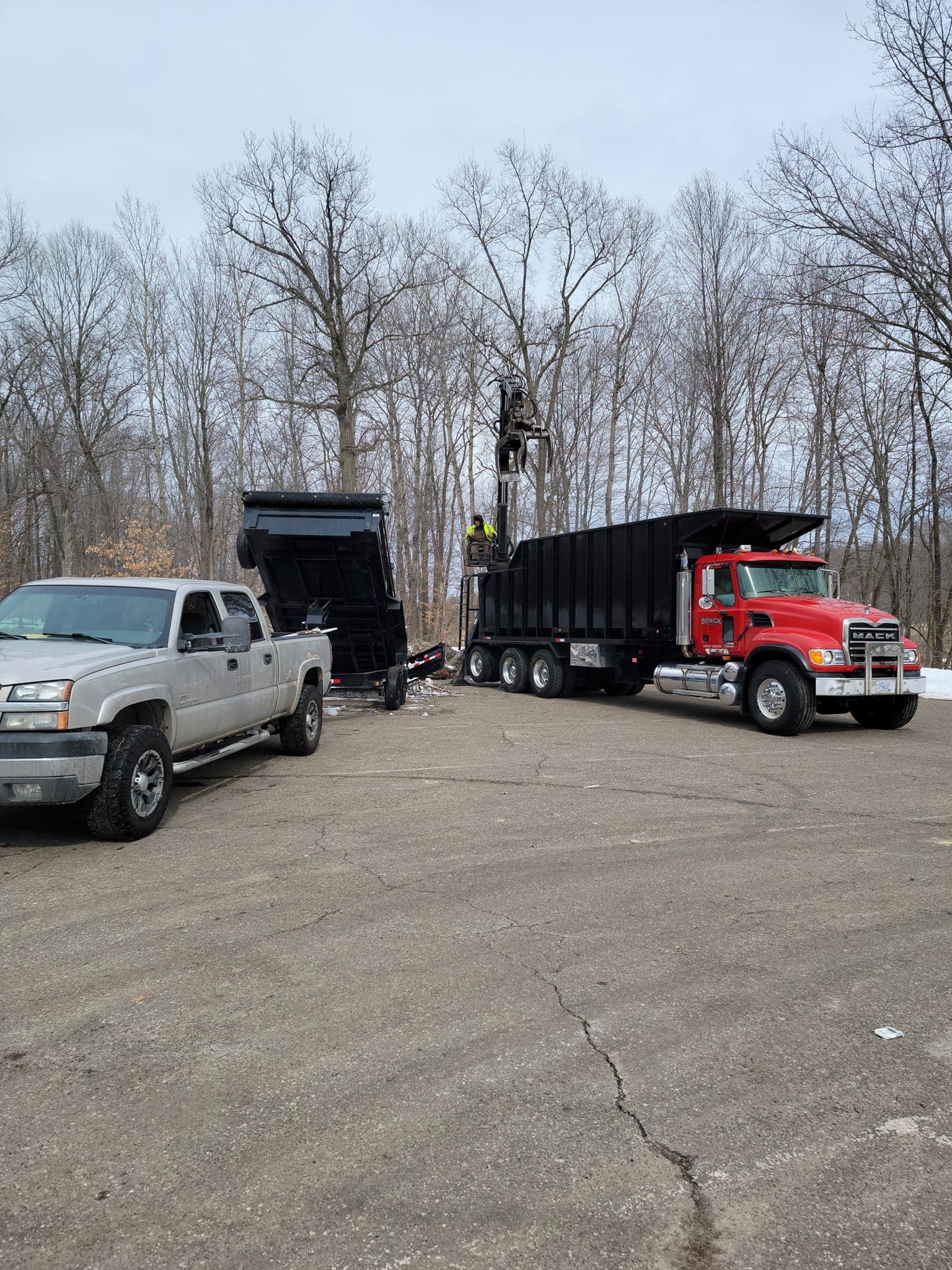 Silver pickup truck and red dump truck with trailers on asphalt in a wintery setting.