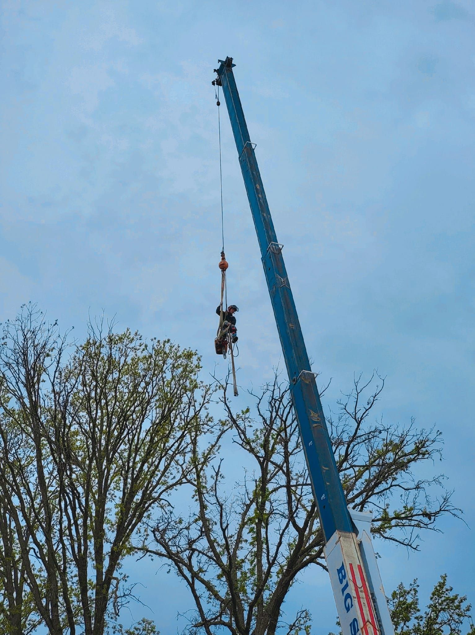 A high ride at an amusement park. The ride is suspended in the air by a crane; cloudy sky in the background.