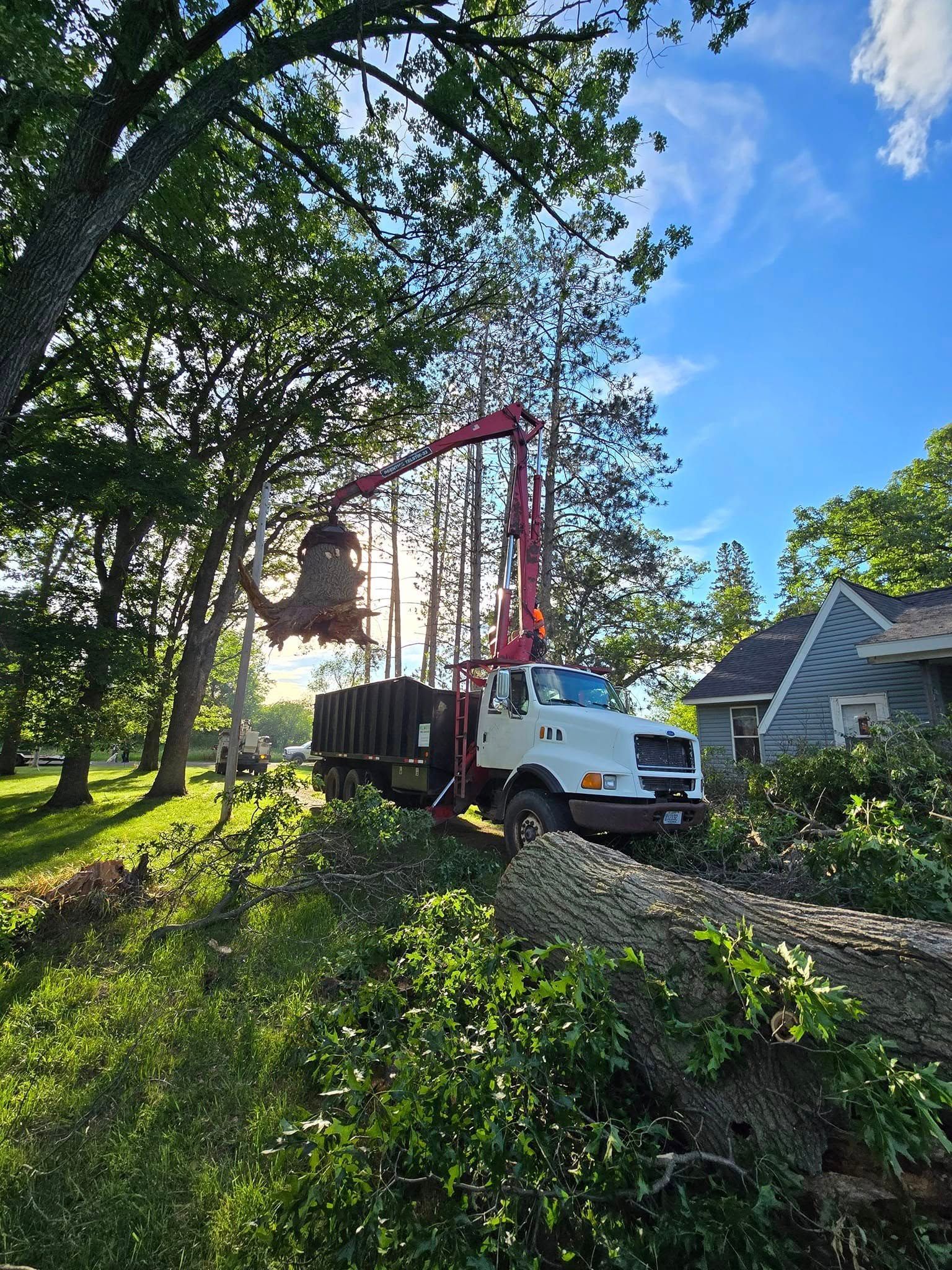 Tree service truck with a crane loading tree debris on a sunny day near a house.