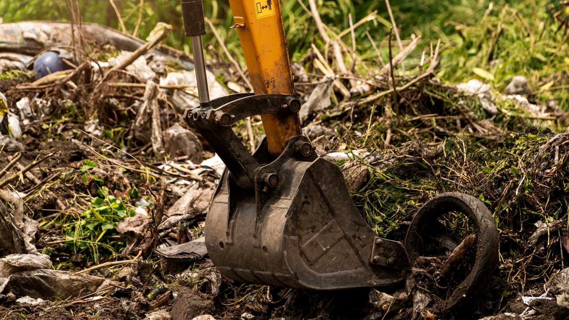 Excavator bucket in mud, surrounded by debris. Yellow arm. Outdoors.