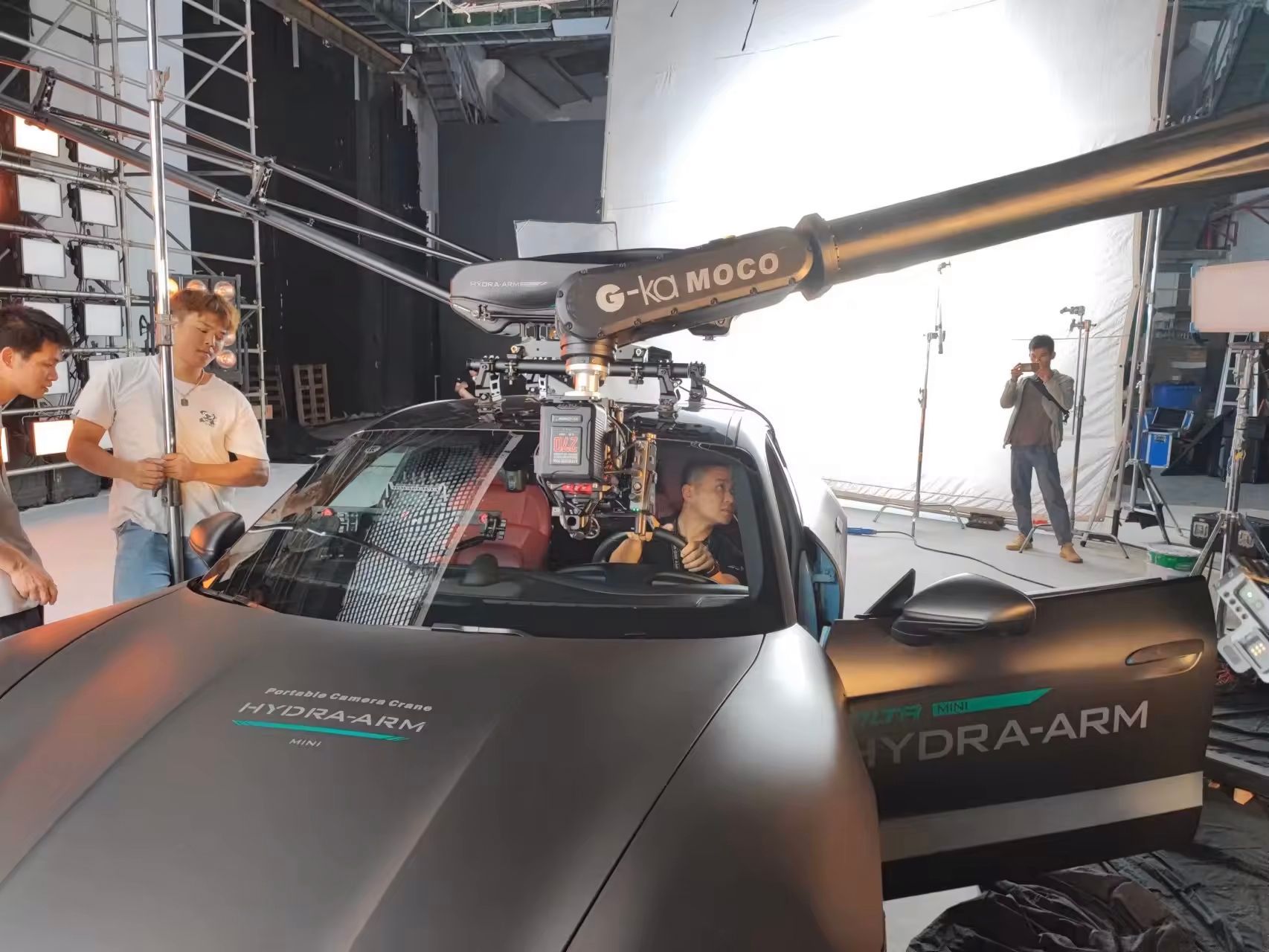 A car is being filmed in a studio with a crane attached to it.