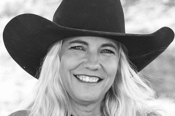 A woman wearing a cowboy hat is smiling in a black and white photo.