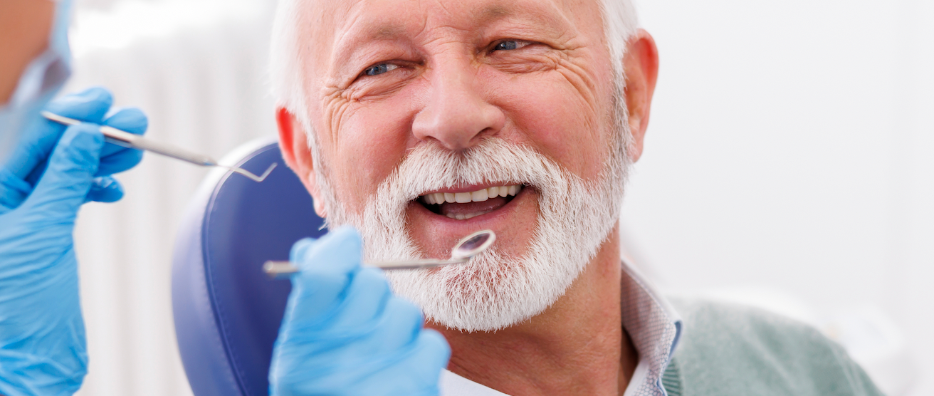 A man with a beard is getting his teeth examined by a dentist.