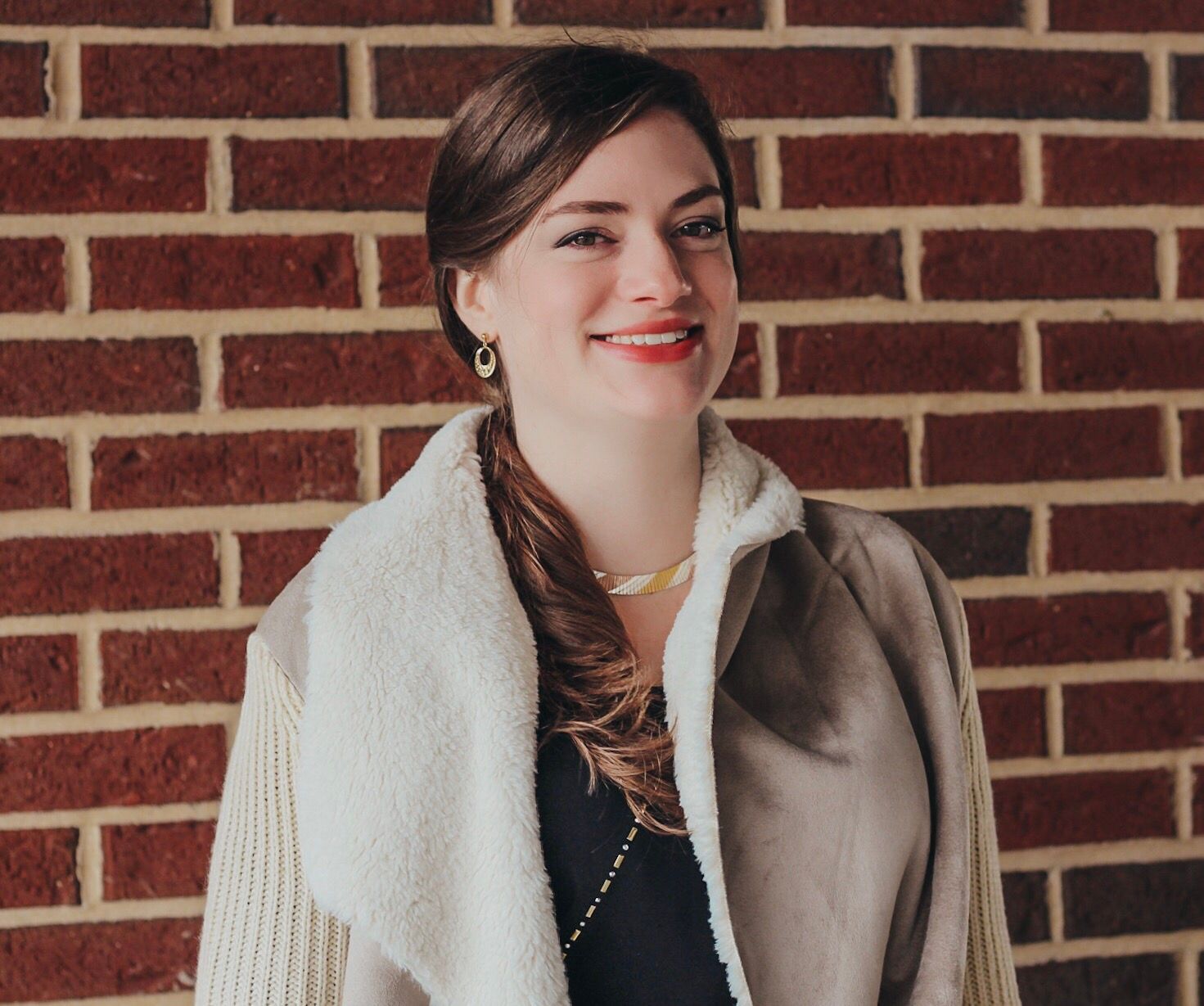 A woman is standing in front of a brick wall and smiling.