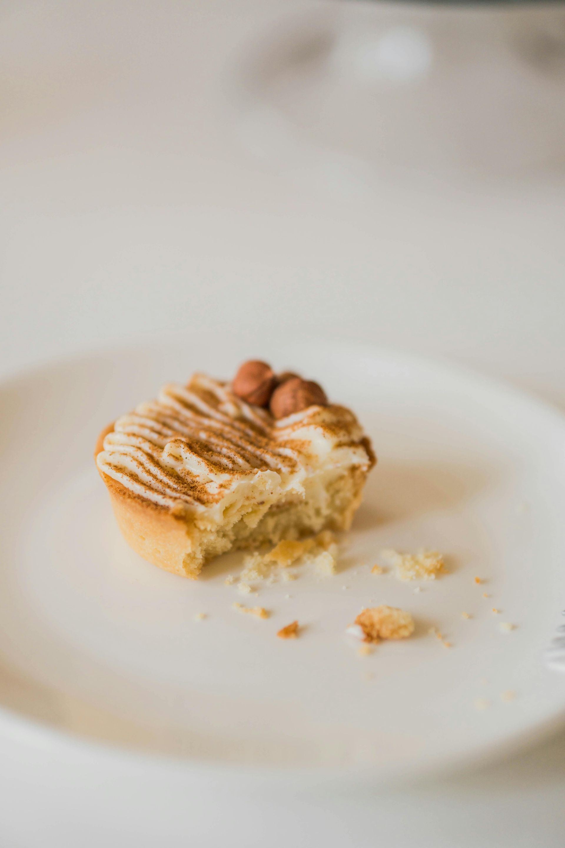 A partially eaten hazelnut tart with piped cream topping rests on a white plate.