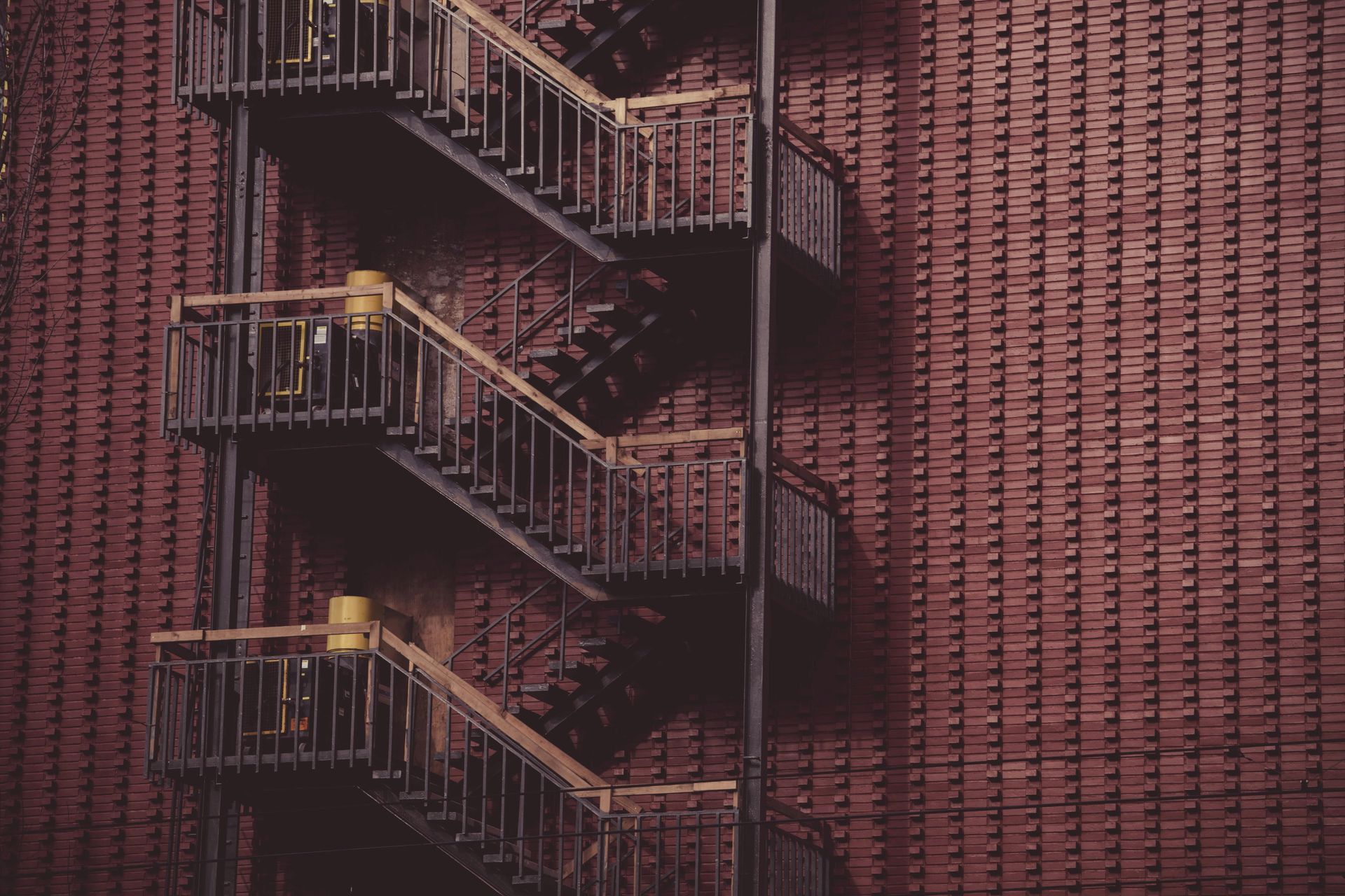 Metal fire escape on a brick building; descending, with three landings, shadowed in evening light.